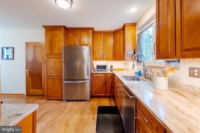 kitchen with light stone counters, stainless steel appliances, light hardwood / wood-style flooring, and sink