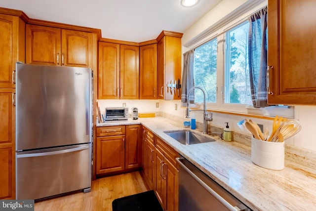 kitchen featuring appliances with stainless steel finishes, light hardwood / wood-style floors, light stone counters, and sink