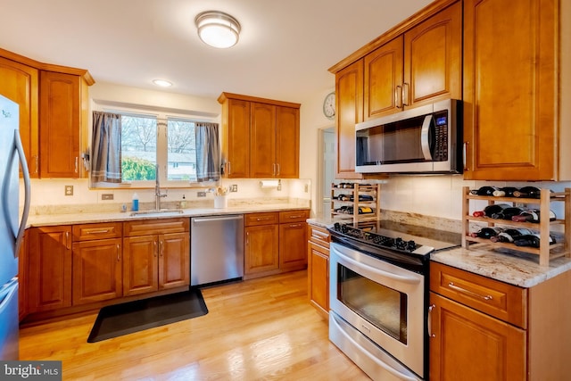 kitchen with backsplash, sink, light wood-type flooring, light stone counters, and stainless steel appliances