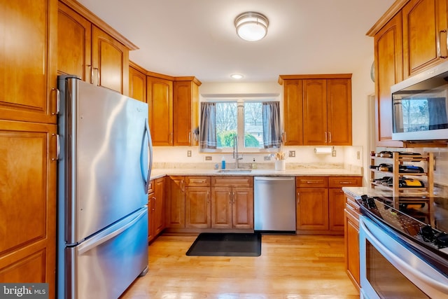 kitchen featuring sink, light stone countertops, stainless steel appliances, and light wood-type flooring