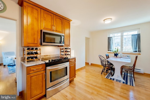 kitchen featuring decorative backsplash, baseboard heating, light hardwood / wood-style floors, light stone counters, and stainless steel appliances