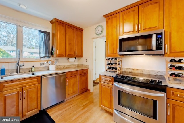 kitchen featuring light wood-type flooring, stainless steel appliances, light stone counters, and sink