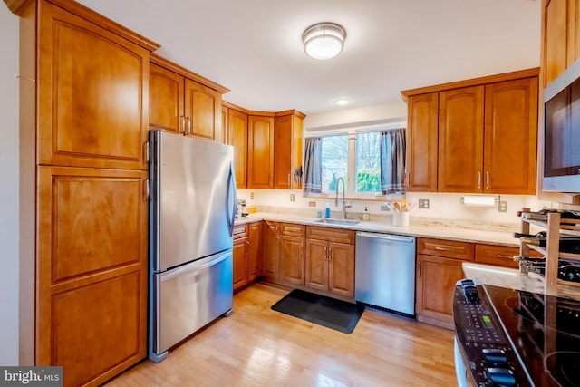 kitchen with light stone counters, sink, stainless steel appliances, and light wood-type flooring