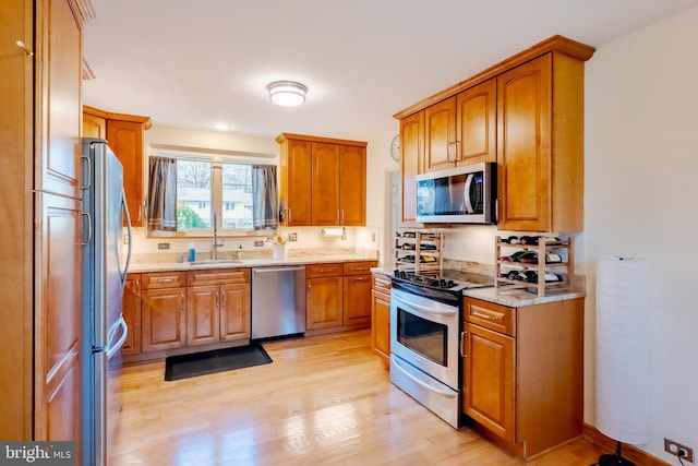 kitchen featuring light stone countertops, sink, stainless steel appliances, and light hardwood / wood-style floors