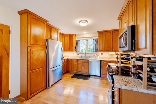 kitchen with light stone countertops, sink, light hardwood / wood-style flooring, and appliances with stainless steel finishes