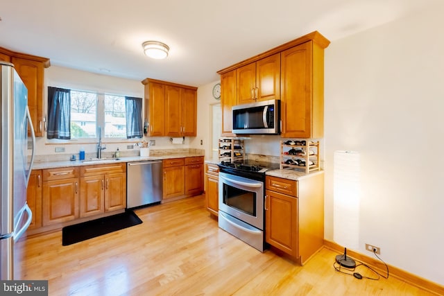 kitchen featuring appliances with stainless steel finishes, light wood-type flooring, light stone counters, and sink