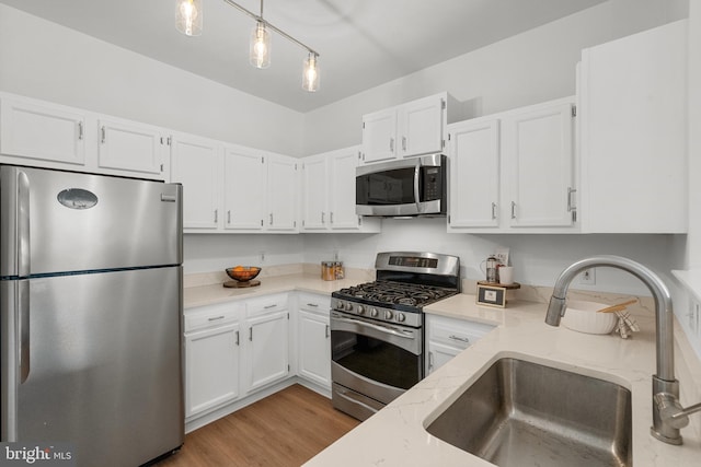 kitchen featuring light wood-type flooring, stainless steel appliances, sink, white cabinets, and hanging light fixtures