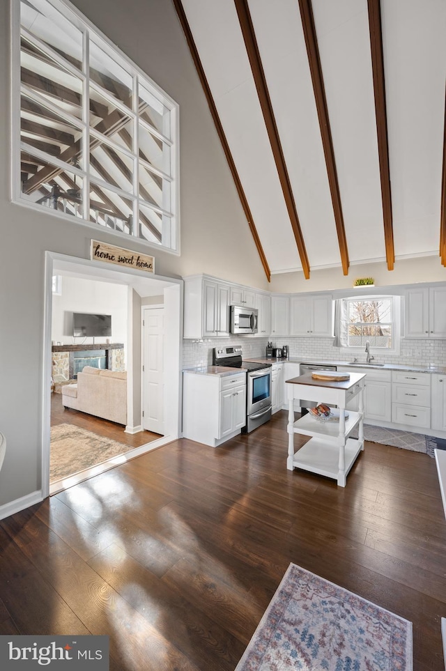 kitchen with decorative backsplash, white cabinets, stainless steel appliances, and high vaulted ceiling