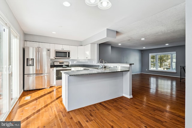 kitchen with kitchen peninsula, appliances with stainless steel finishes, white cabinets, and wood-type flooring