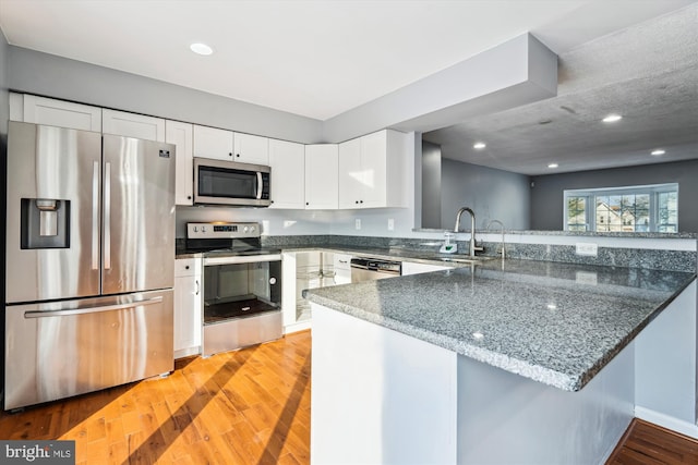 kitchen featuring white cabinetry, sink, kitchen peninsula, dark stone counters, and appliances with stainless steel finishes