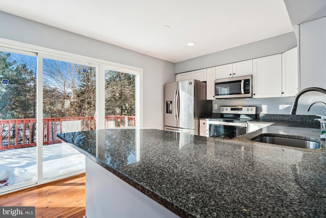 kitchen with light wood-type flooring, dark stone counters, stainless steel appliances, sink, and white cabinets