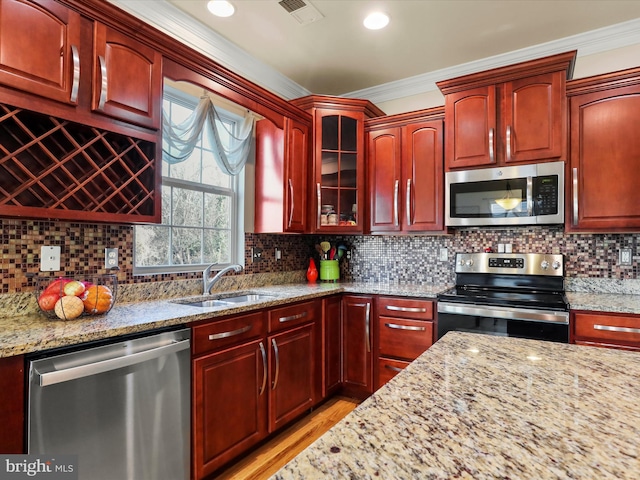 kitchen featuring light stone countertops, appliances with stainless steel finishes, backsplash, crown molding, and sink