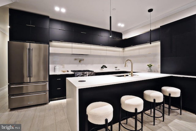 kitchen with light hardwood / wood-style floors, high end fridge, a breakfast bar area, hanging light fixtures, and sink