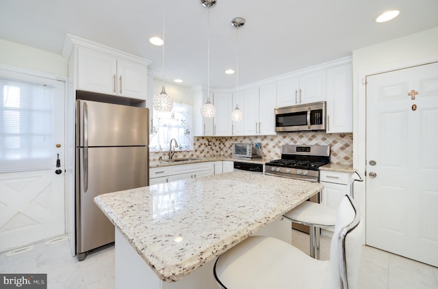 kitchen with sink, stainless steel appliances, a kitchen island, decorative light fixtures, and white cabinets