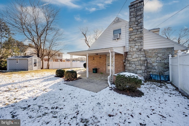 snow covered property featuring cooling unit, a storage shed, and a patio area