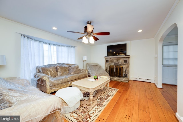 living room featuring ceiling fan, a baseboard radiator, a stone fireplace, hardwood / wood-style floors, and ornamental molding