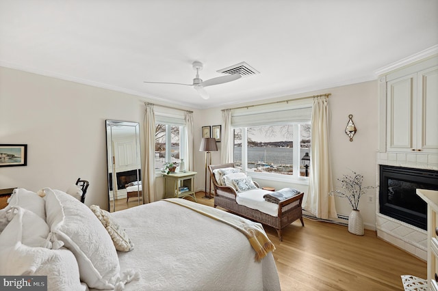 bedroom with ceiling fan, a baseboard radiator, light hardwood / wood-style floors, a fireplace, and ornamental molding