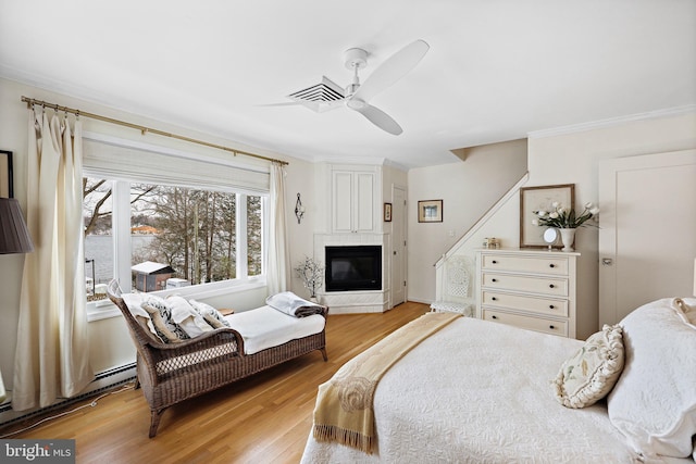 bedroom featuring ceiling fan, light wood-type flooring, crown molding, and a baseboard radiator