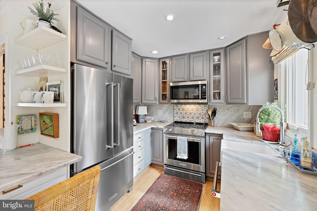 kitchen with light stone countertops, appliances with stainless steel finishes, backsplash, light wood-type flooring, and gray cabinets