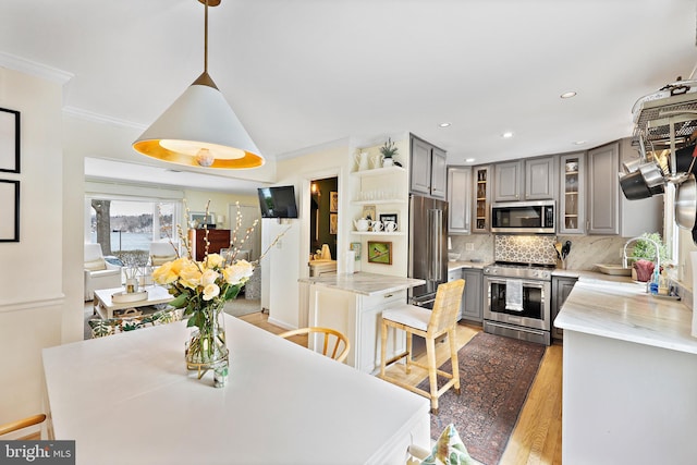 kitchen featuring dark hardwood / wood-style flooring, pendant lighting, gray cabinets, decorative backsplash, and appliances with stainless steel finishes