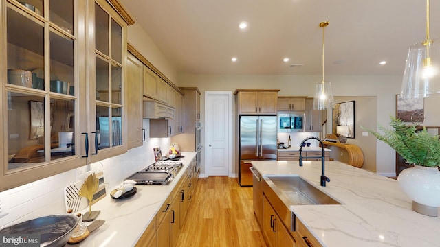 kitchen featuring premium range hood, stainless steel appliances, sink, light hardwood / wood-style floors, and hanging light fixtures