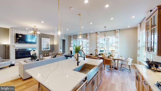 kitchen featuring light stone counters, light wood-type flooring, a kitchen island with sink, and a wealth of natural light