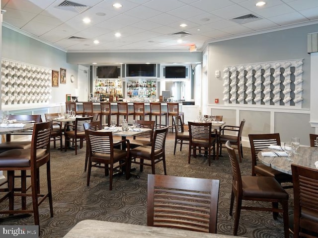 dining space featuring ornamental molding, a drop ceiling, and dark colored carpet