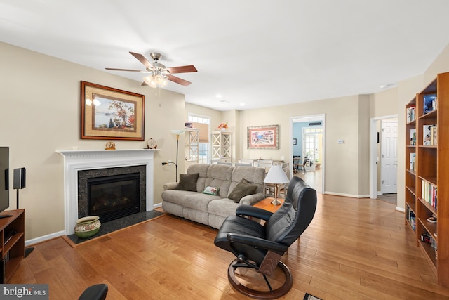 living room featuring ceiling fan, plenty of natural light, a fireplace, and light hardwood / wood-style flooring