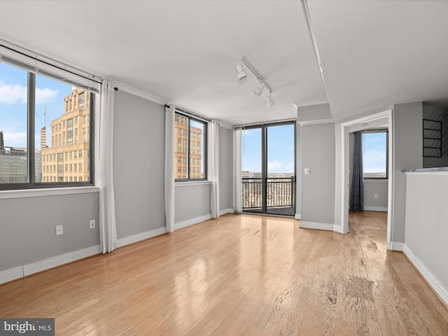 empty room with plenty of natural light, track lighting, and light hardwood / wood-style flooring