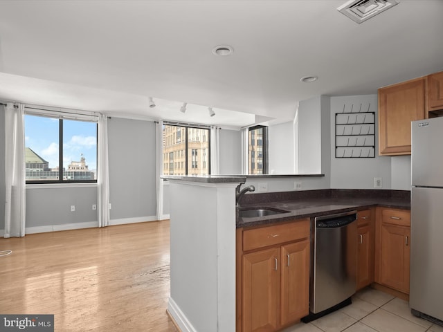 kitchen with kitchen peninsula, stainless steel appliances, sink, light tile patterned floors, and dark stone countertops