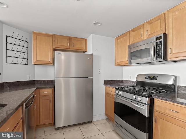 kitchen featuring light tile patterned floors, stainless steel appliances, and dark stone counters