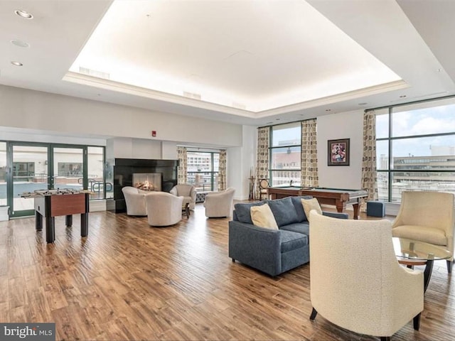 living room featuring a raised ceiling, a tiled fireplace, wood-type flooring, and pool table