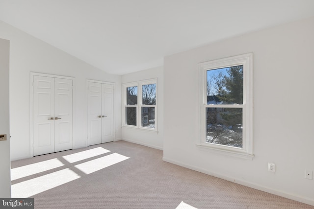 unfurnished bedroom with lofted ceiling, two closets, and light carpet