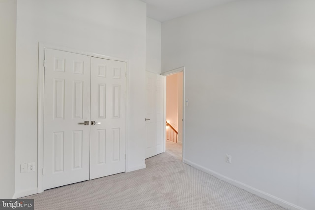 unfurnished bedroom featuring a high ceiling, light colored carpet, and a closet