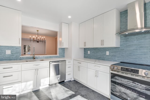 kitchen with stainless steel appliances, sink, white cabinets, wall chimney exhaust hood, and a chandelier