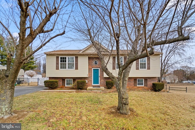 bi-level home with brick siding, a front lawn, fence, and aphalt driveway