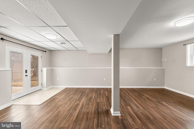 basement with dark wood-style floors, baseboards, a drop ceiling, and french doors