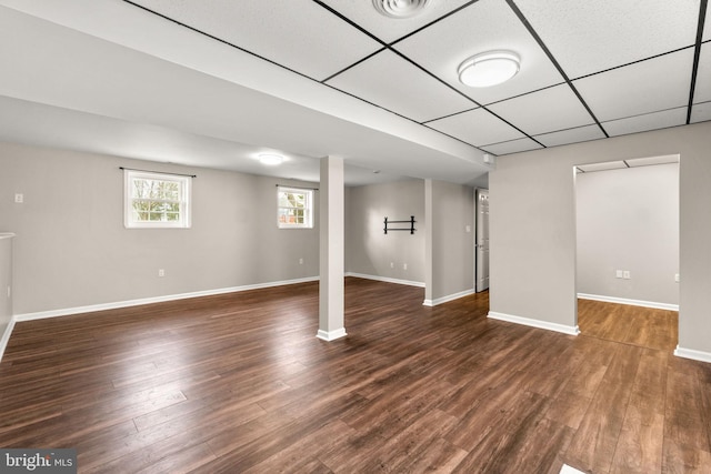 below grade area with dark wood-style floors, a paneled ceiling, and baseboards