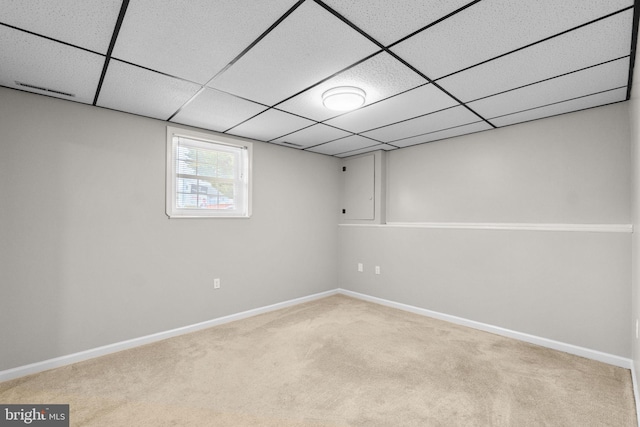 below grade area with a paneled ceiling, light carpet, and baseboards