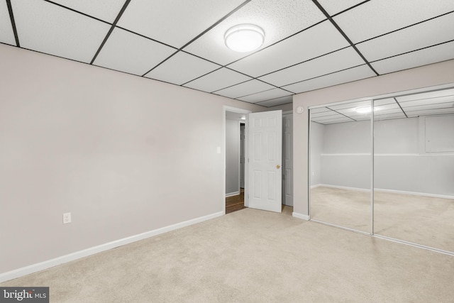 unfurnished bedroom featuring a paneled ceiling, a closet, light carpet, and baseboards