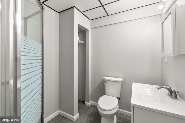 bathroom featuring toilet, baseboards, a drop ceiling, and vanity