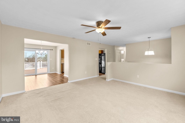 carpeted spare room featuring visible vents, baseboards, and ceiling fan with notable chandelier