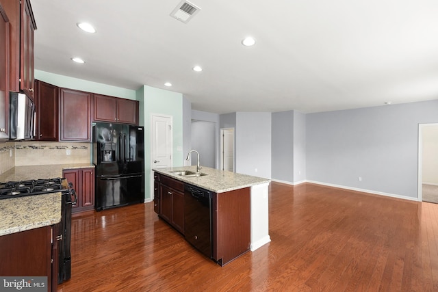 kitchen featuring black appliances, a center island with sink, sink, decorative backsplash, and light stone counters