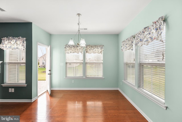 unfurnished dining area with wood-type flooring, a notable chandelier, and a healthy amount of sunlight