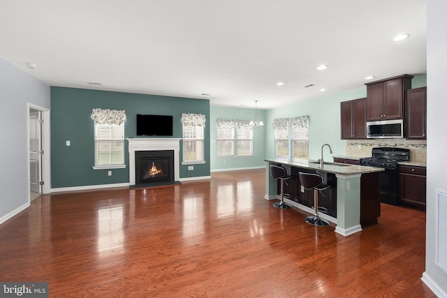 kitchen with dark brown cabinetry, black range with gas stovetop, a breakfast bar area, decorative backsplash, and a center island with sink