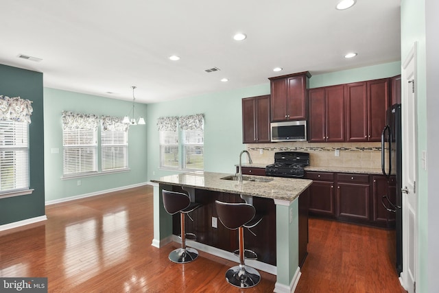 kitchen featuring light stone countertops, sink, an island with sink, pendant lighting, and black appliances