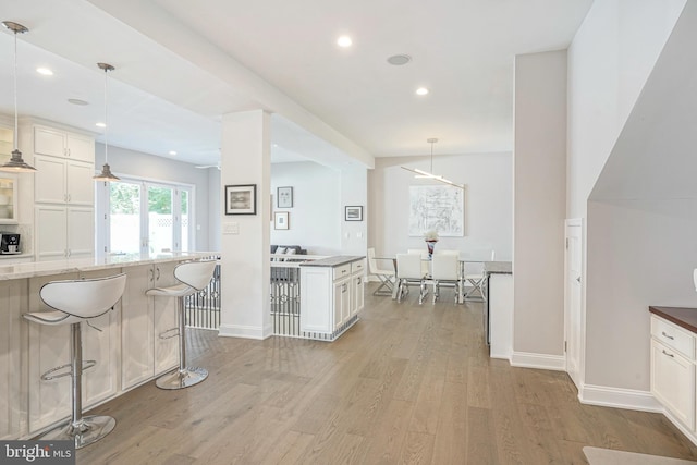 kitchen with light stone counters, light hardwood / wood-style flooring, white cabinetry, hanging light fixtures, and a breakfast bar area