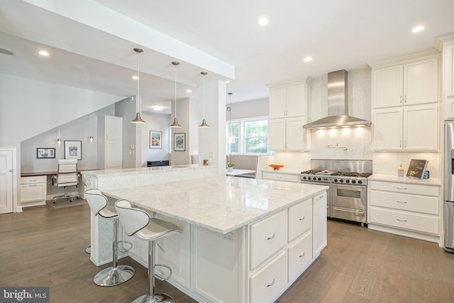 kitchen featuring wall chimney exhaust hood, light stone counters, backsplash, white cabinets, and appliances with stainless steel finishes