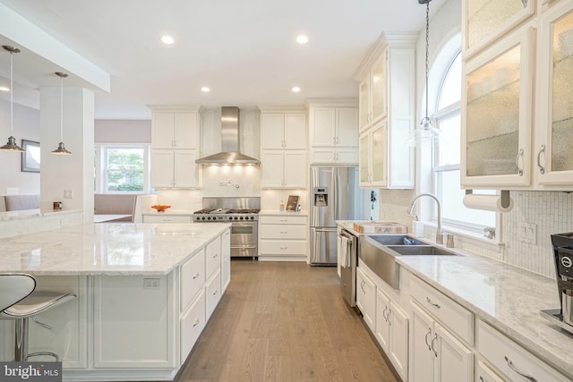 kitchen featuring backsplash, wall chimney range hood, appliances with stainless steel finishes, decorative light fixtures, and white cabinetry