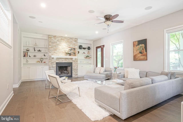 living room with a fireplace, built in shelves, hardwood / wood-style flooring, and ceiling fan